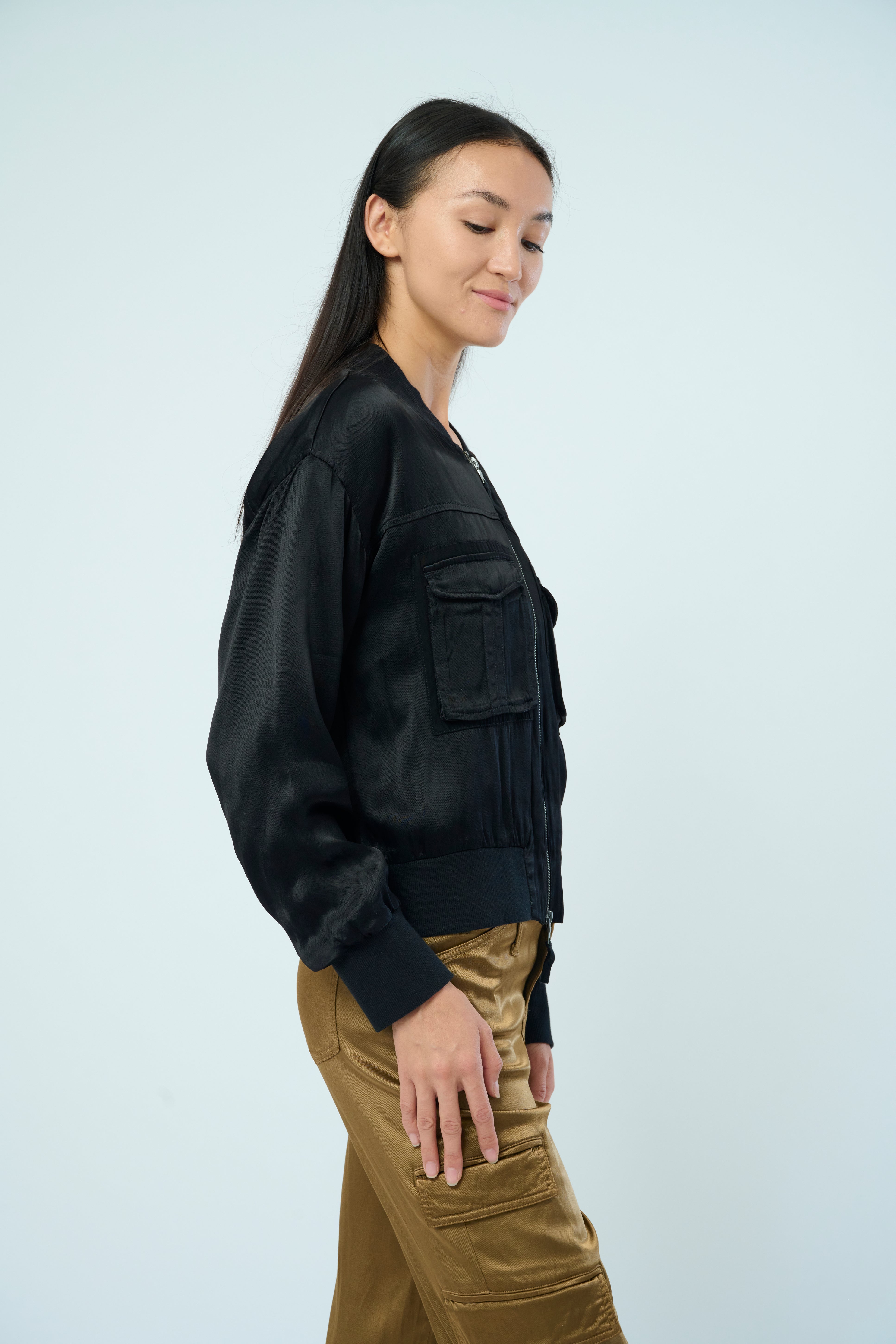 Side view of a tall female model with long black hair confidently posing wearing our black colored Dazie flight jacket from Marrakech Clothing.