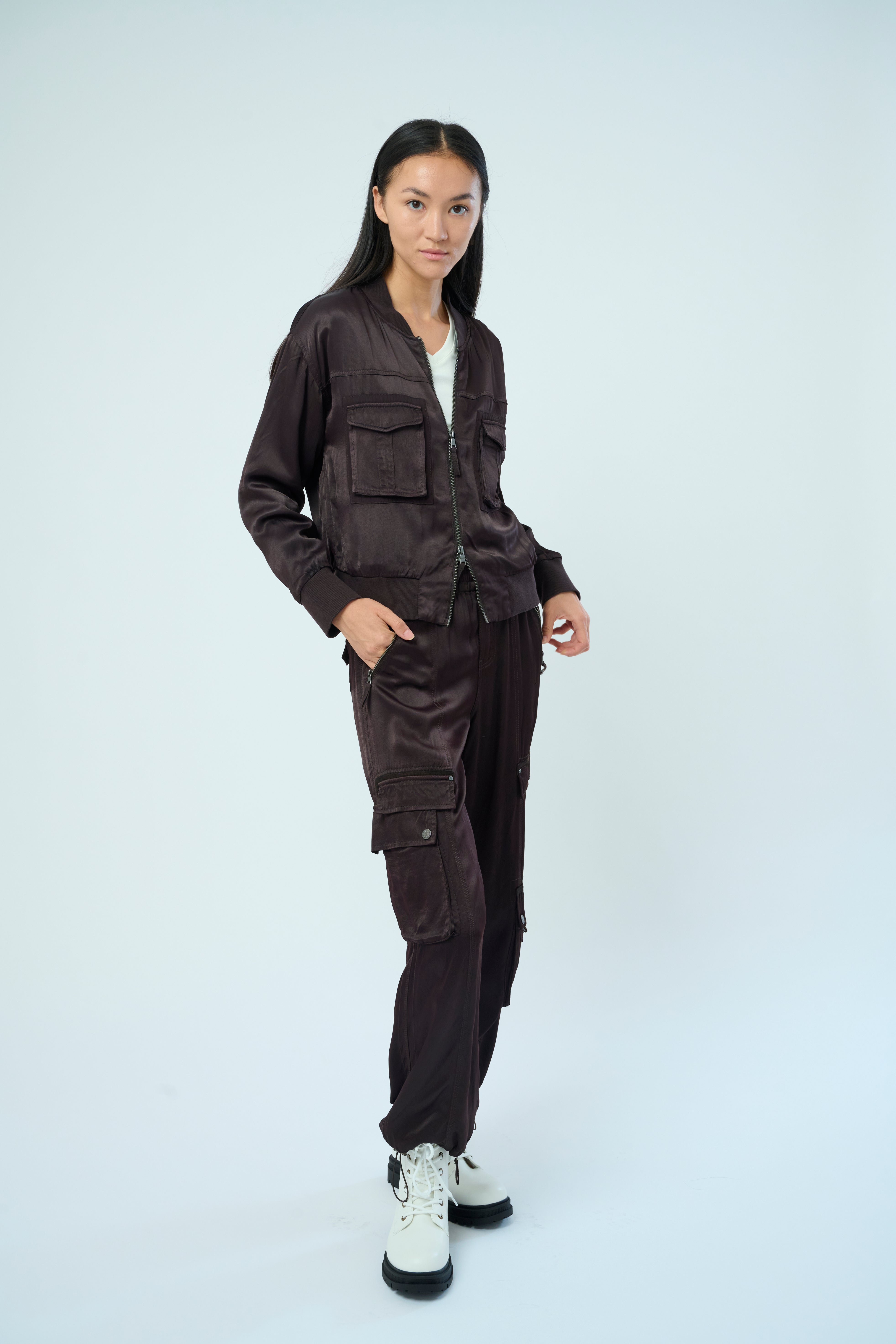 Front view of a tall female model with long black hair confidently posing wearing our dark chocolate colored Enika Viscose Satin Twill Cargo Jogger pant from Marrakech Clothing.