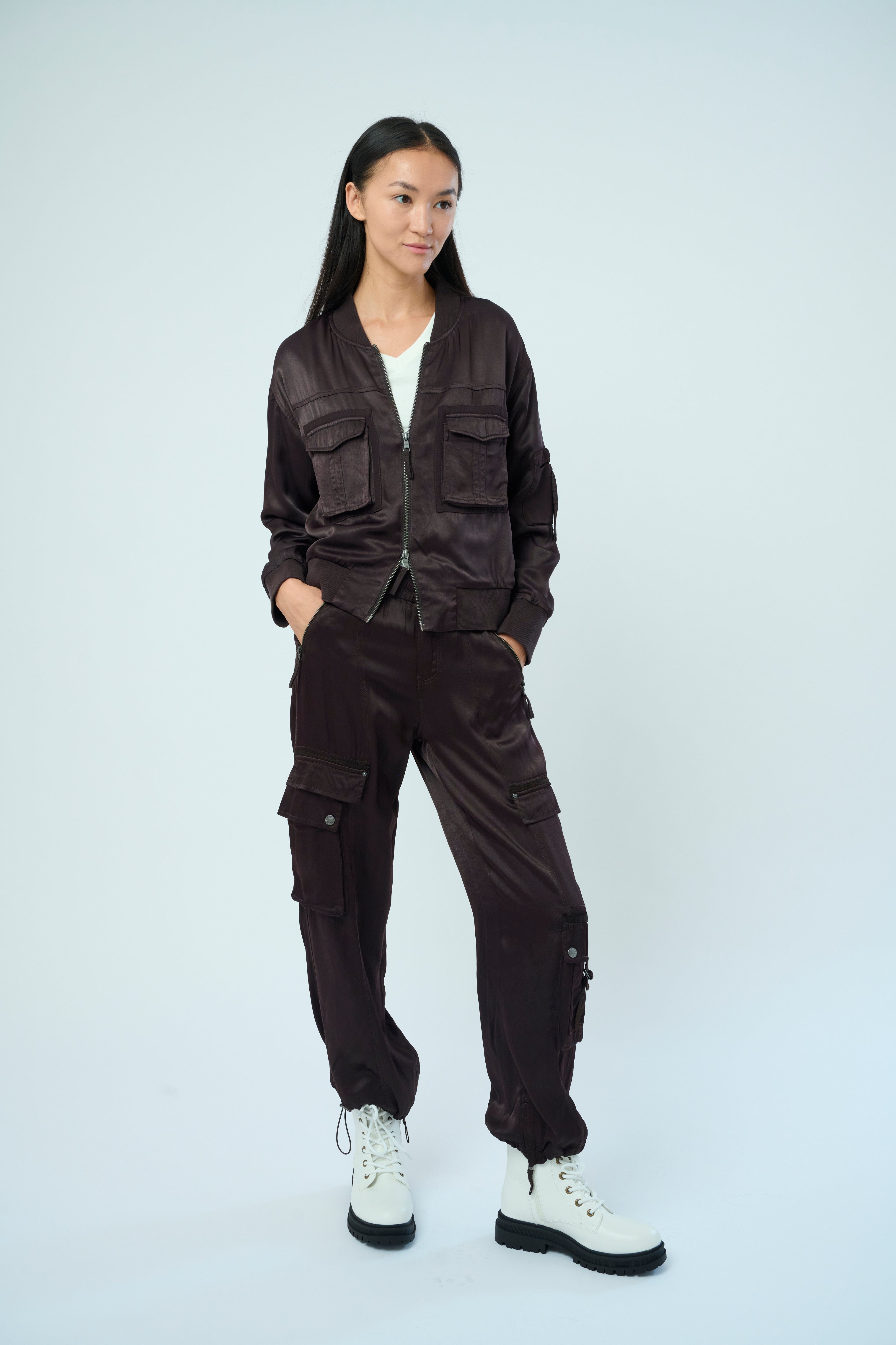 A tall female model with long black hair confidently posing wearing our dark chocolate colored Dazie flight jacket with a brown zipper from Marrakech Clothing.