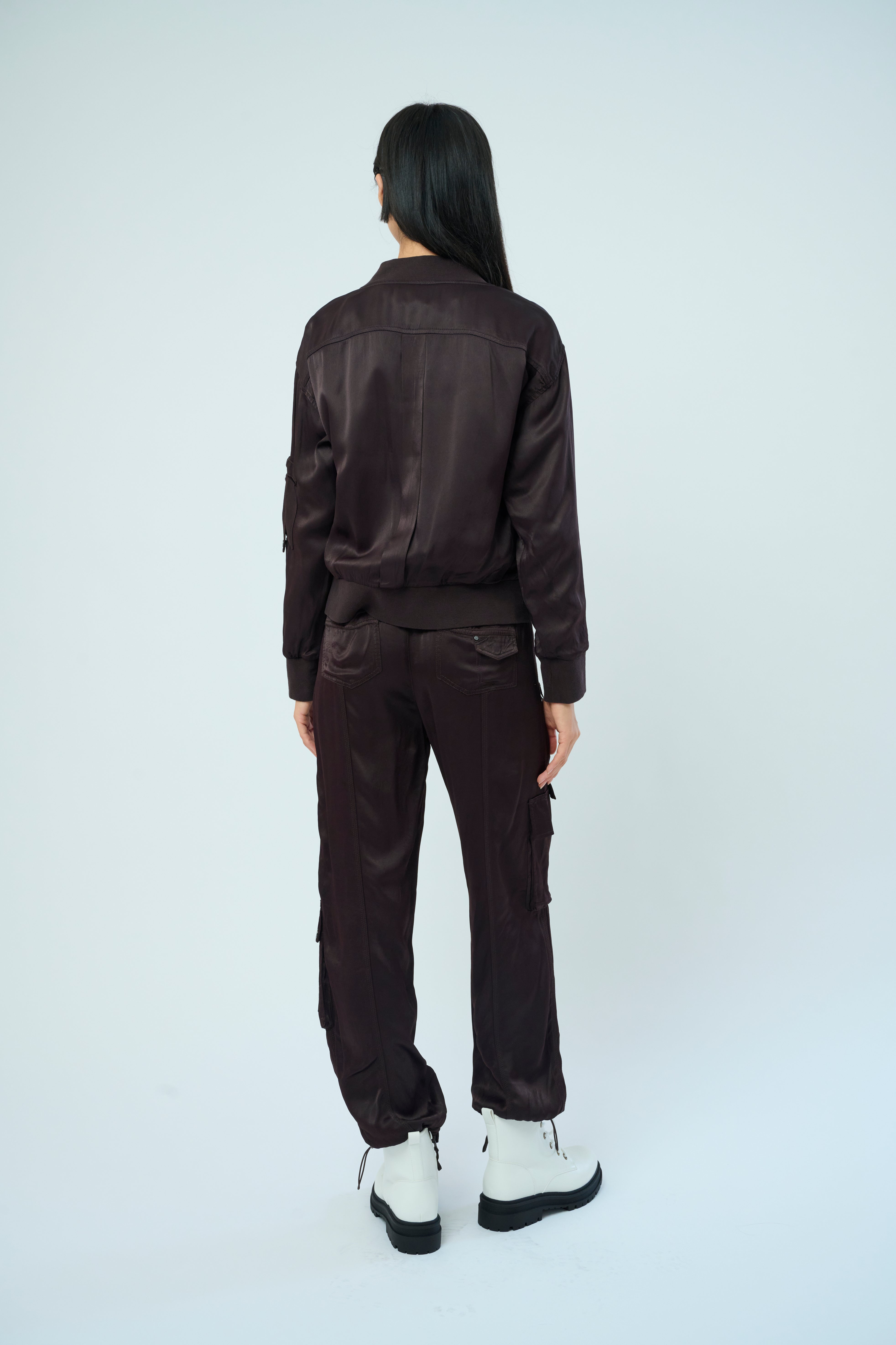 Back view of a tall female model with long black hair confidently posing wearing our dark chocolate colored Dazie flight jacket with a brown zipper from Marrakech Clothing.