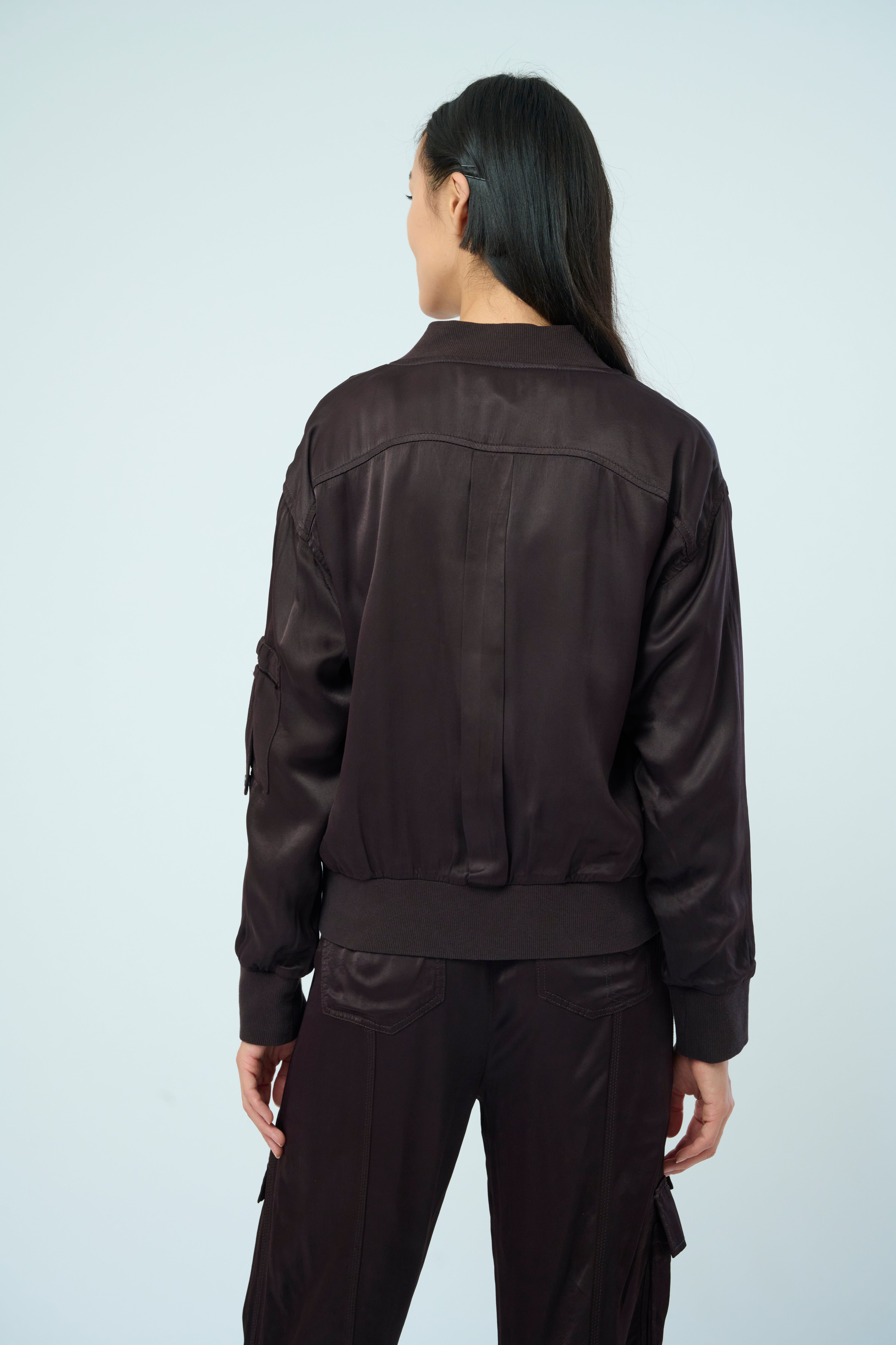 Back view of a tall female model with long black hair confidently posing wearing our dark chocolate colored Dazie flight jacket with a brown zipper from Marrakech Clothing.