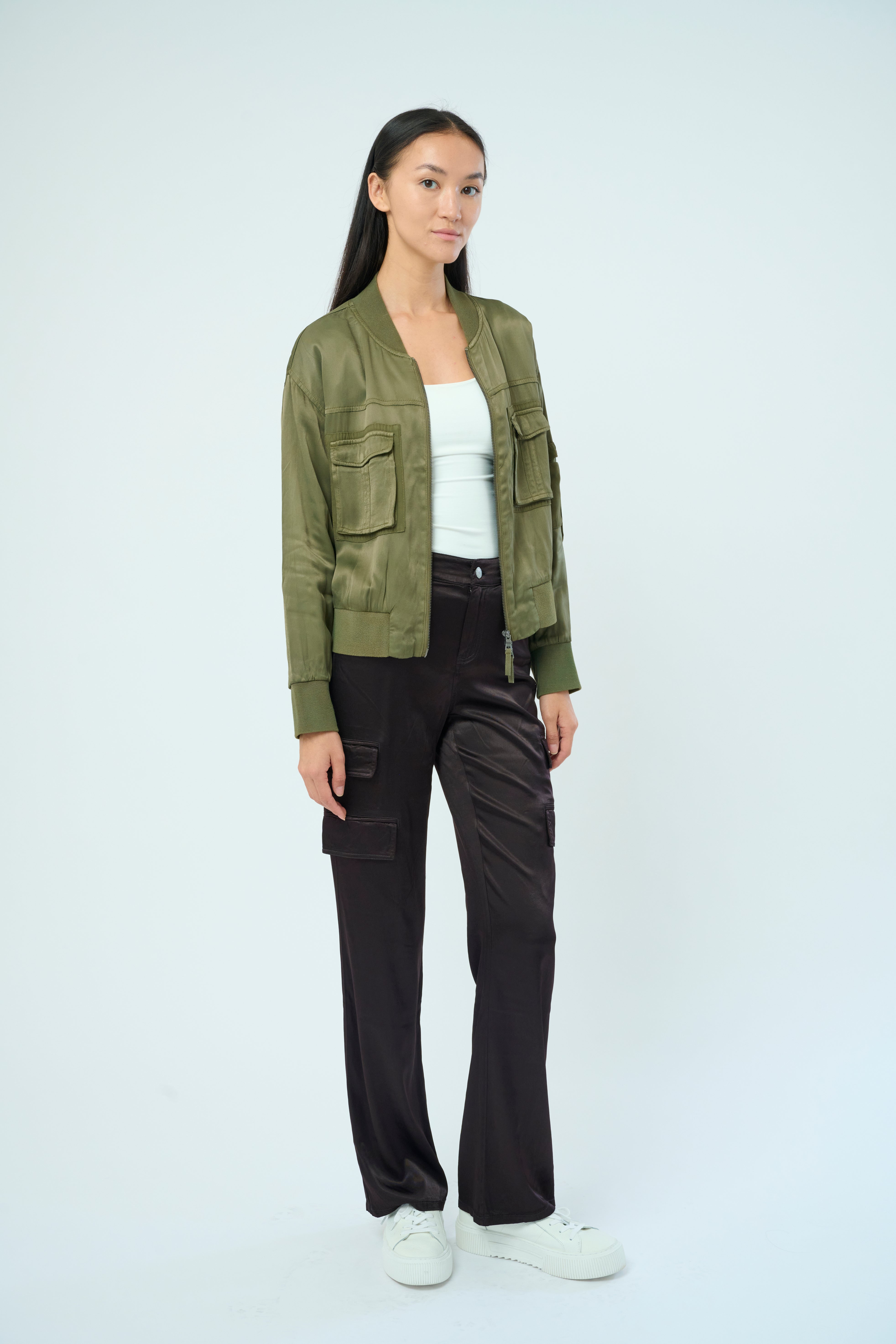 Front view of a tall female model with long black hair confidently posing wearing our pine colored Dazie flight jacket from Marrakech Clothing.