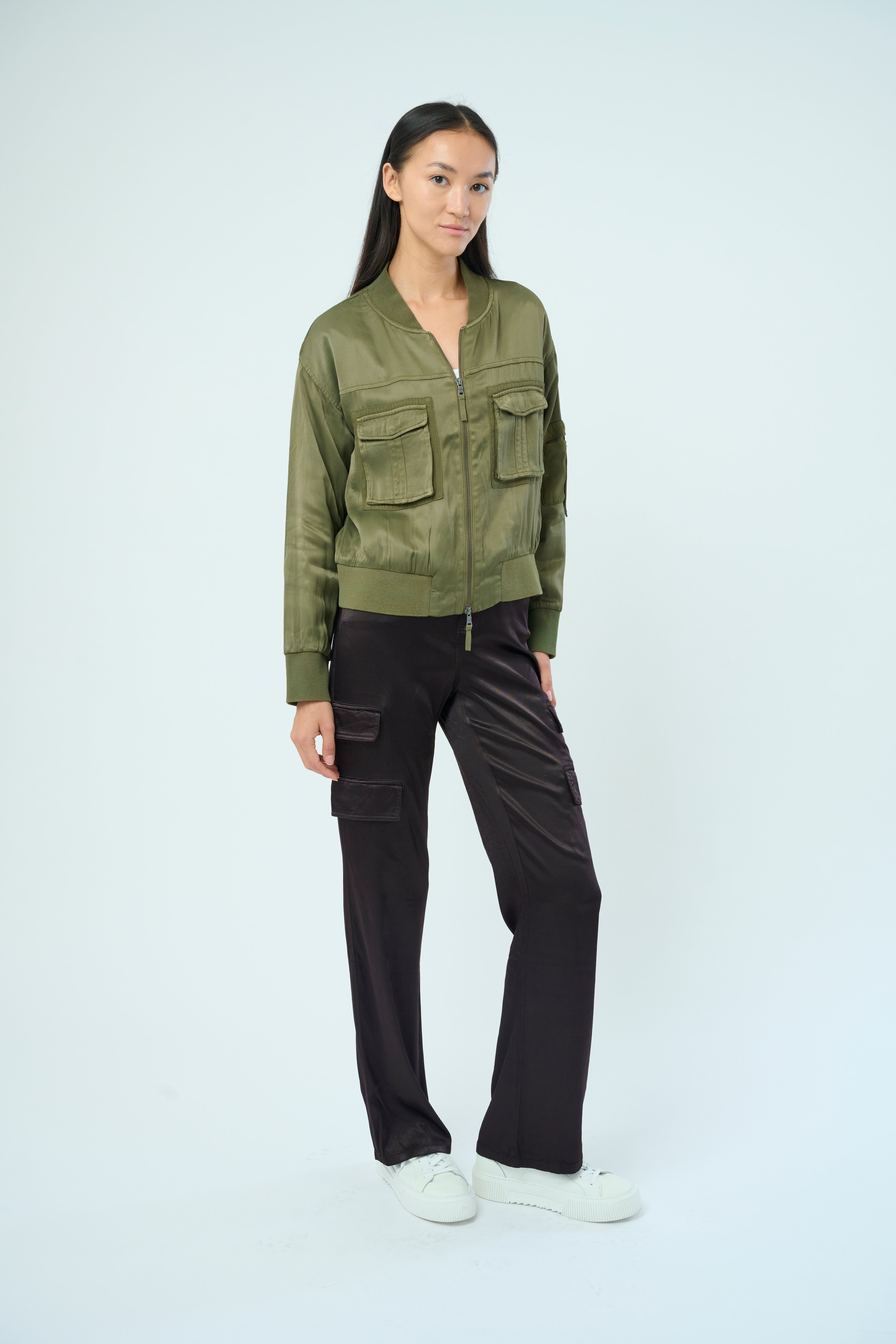 Front view of a tall female model with long black hair confidently posing wearing our pine colored Dazie flight jacket from Marrakech Clothing.