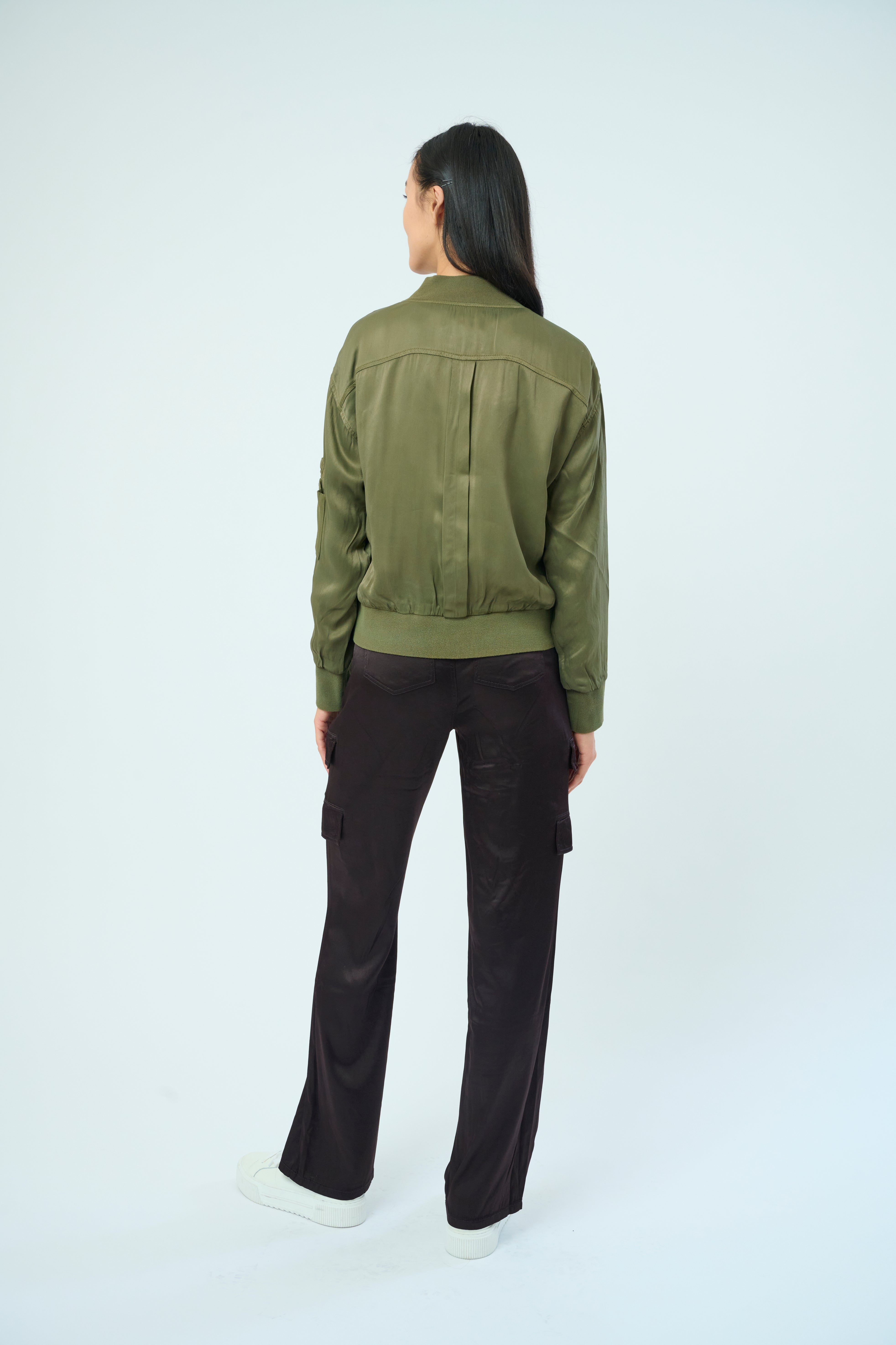 Back view of a tall female model with long black hair confidently posing wearing our pine colored Dazie flight jacket from Marrakech Clothing.