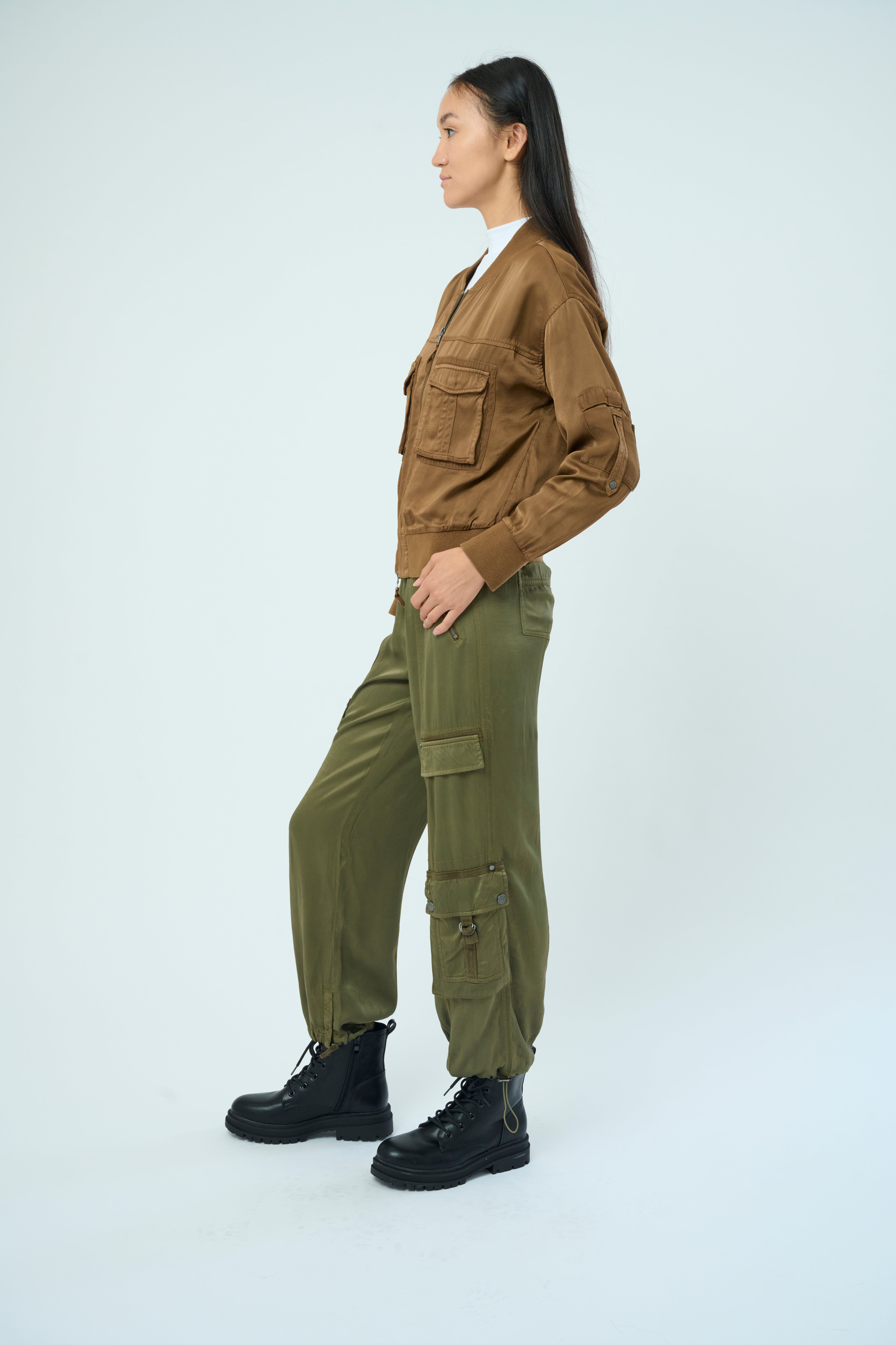 Side view of a tall female model with long black hair confidently posing with hands in pockets, wearing our cheetah colored Dazie flight jacket with a brown zipper from Marrakech Clothing.