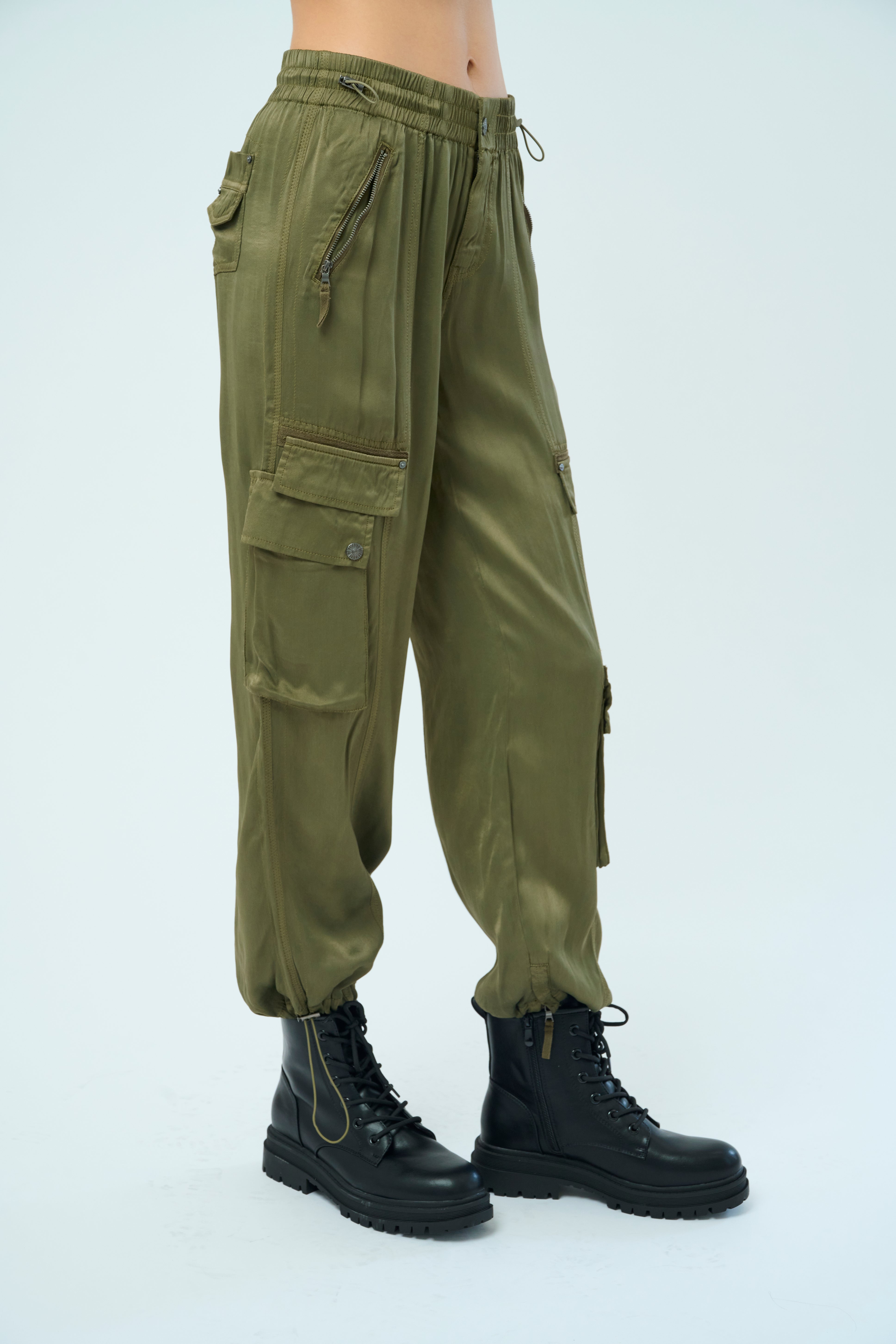 Closeup side view of a tall female model with long black hair confidently posing wearing our pine colored Enika Viscose Satin Twill Cargo Jogger pant from Marrakech Clothing.