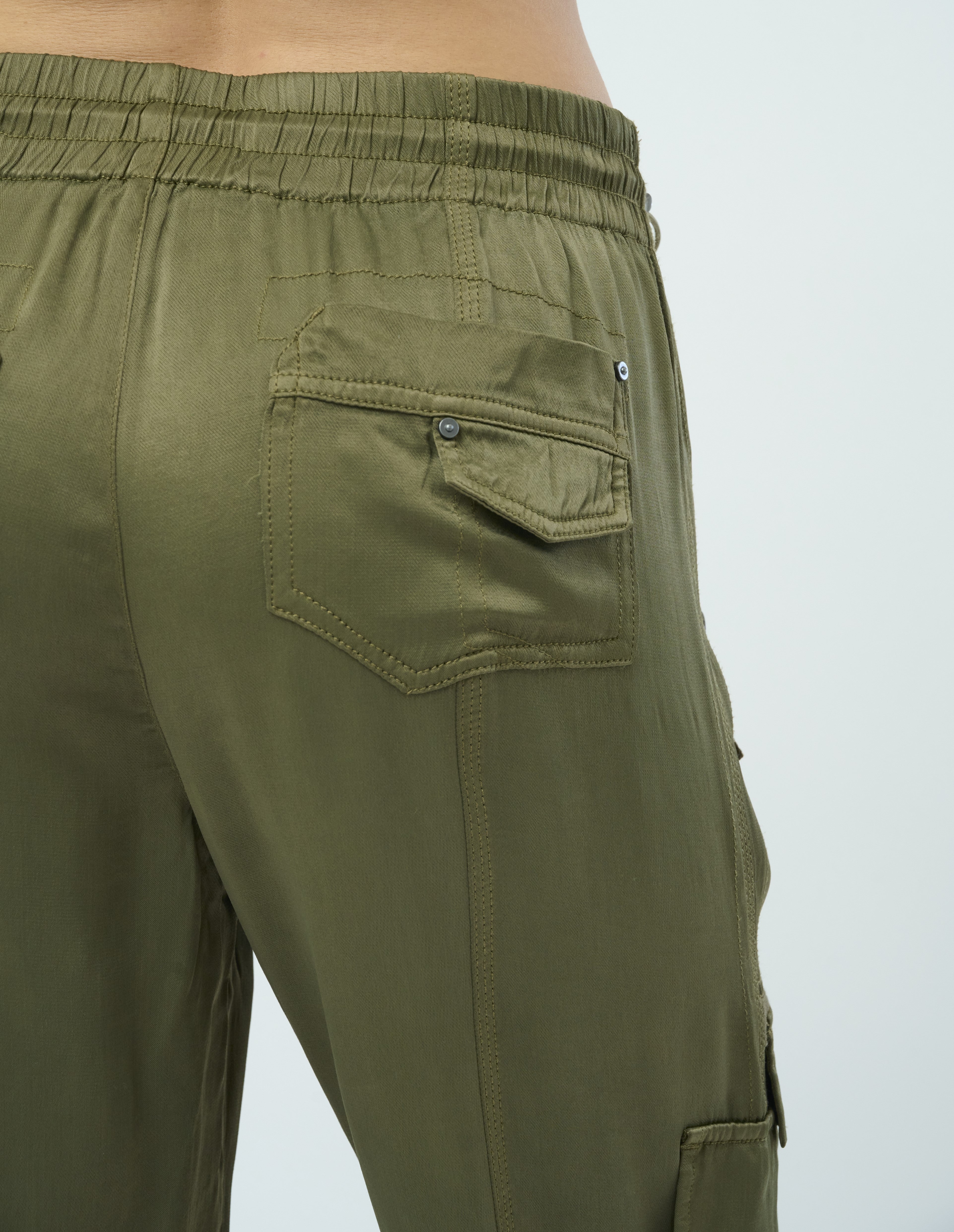 Closeup back detail of a tall female model confidently posing wearing our pine colored Enika Viscose Satin Twill Cargo Jogger pant from Marrakech Clothing.