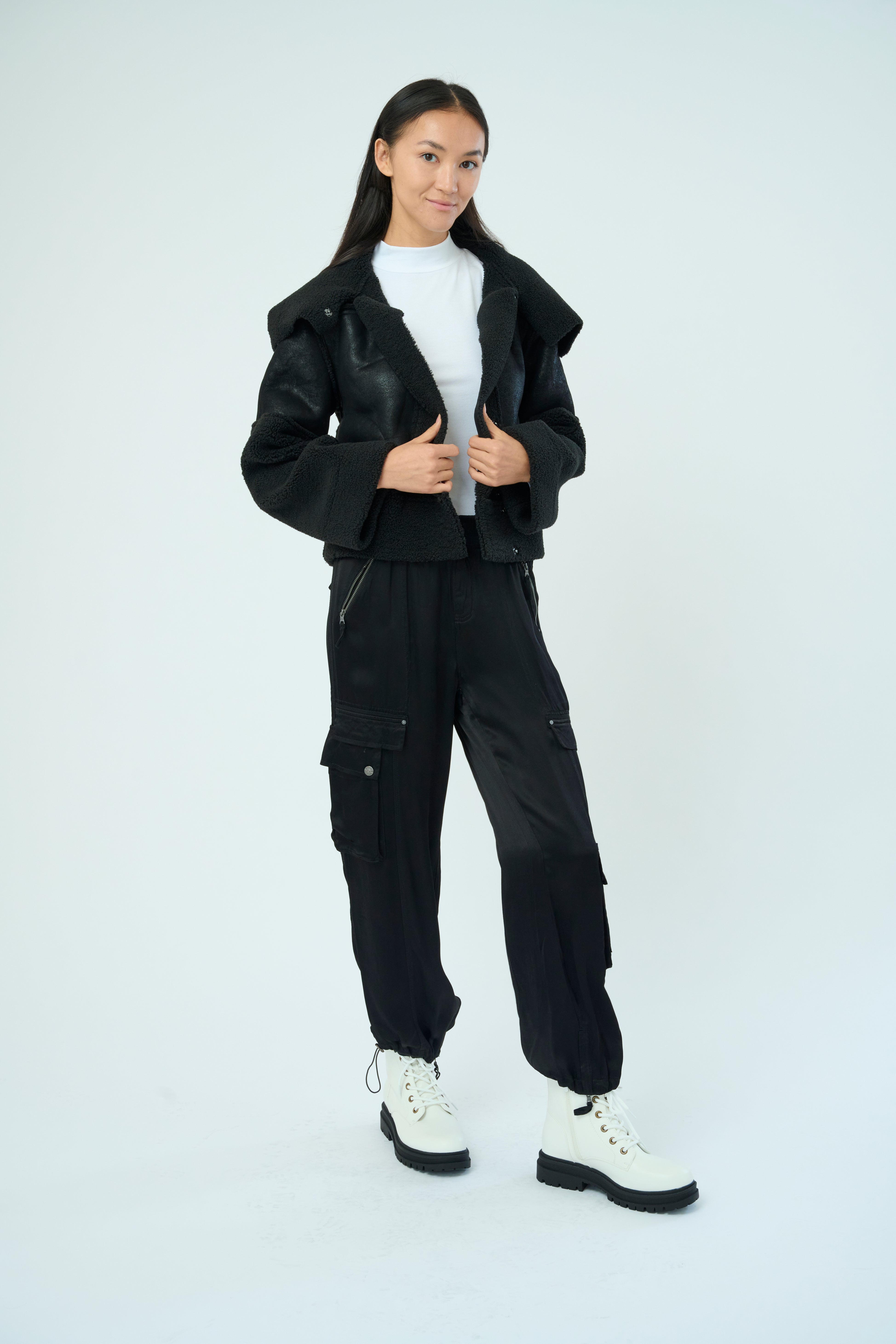 Front view of a tall female model with long black hair confidently posing wearing our black colored Enika Viscose Satin Twill Cargo Jogger pant from Marrakech Clothing.