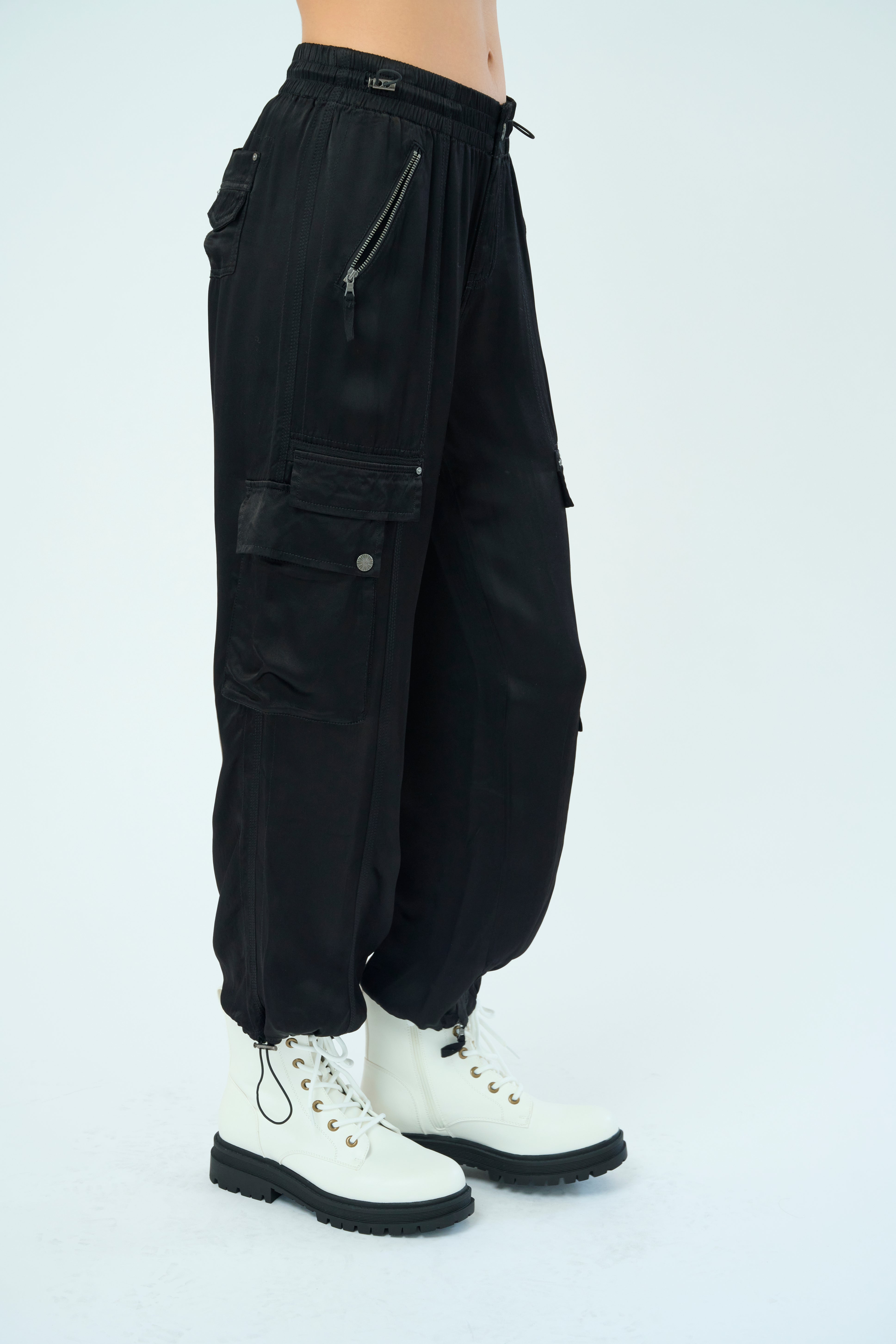 Side view of a tall female model confidently posing wearing our black colored Enika Viscose Satin Twill Cargo Jogger pant from Marrakech Clothing.