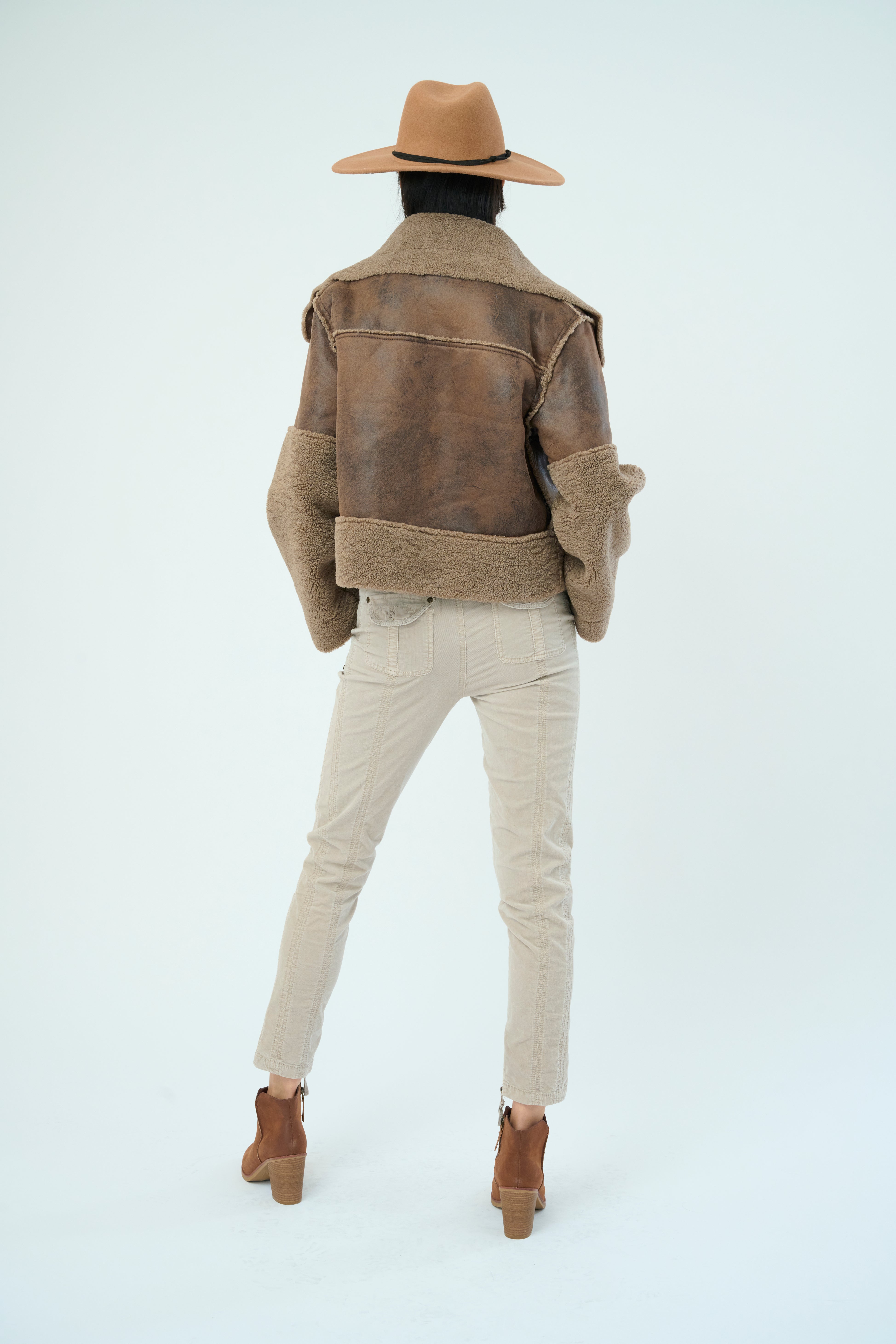 Back view of a tall female model with long black hair confidently posing wearing our hazel colored Trisha Bonded Distressed Suede Sherpa Jacket from Marrakech Clothing.