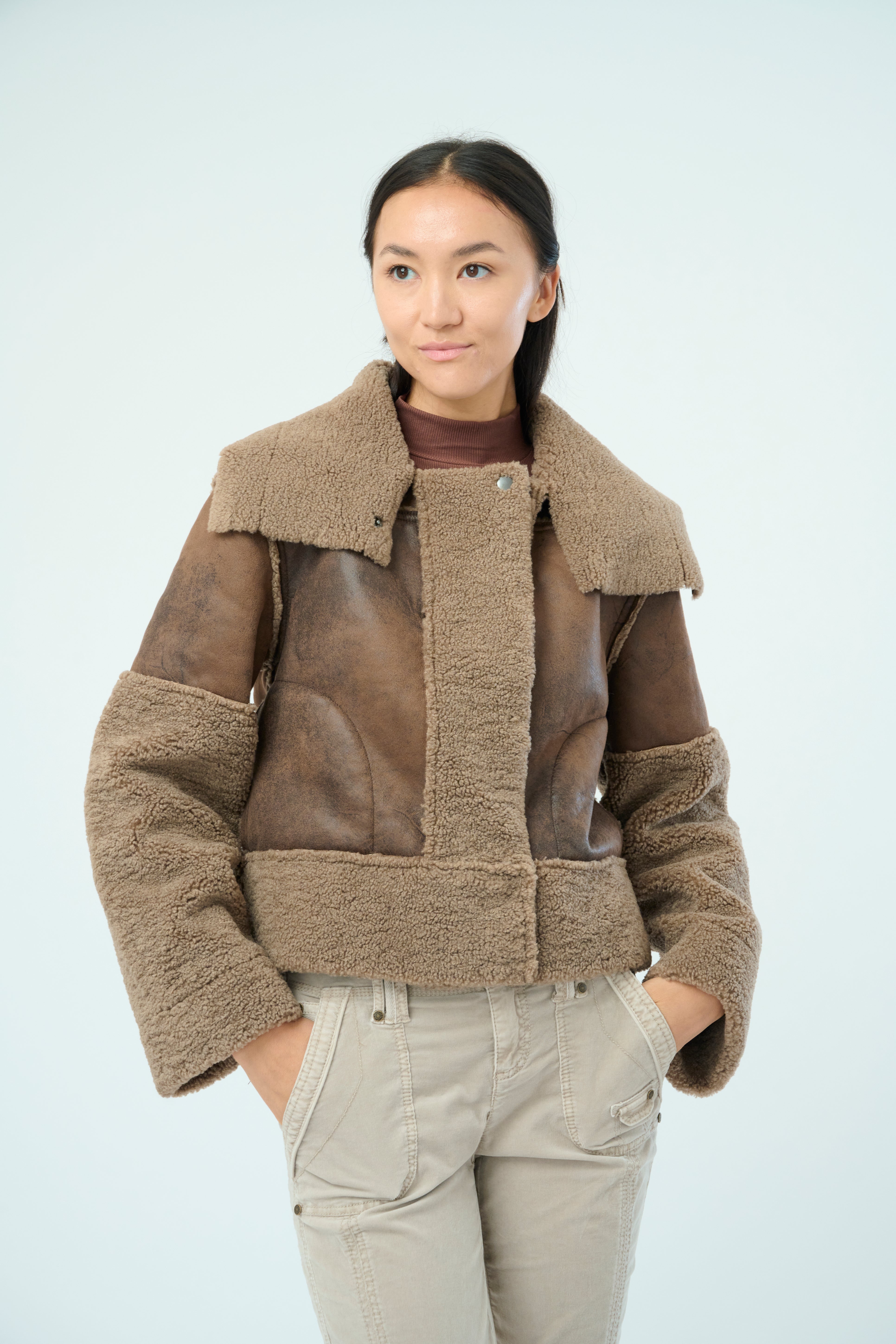 Front view of a tall female model with long black hair confidently posing wearing our hazel colored Trisha Bonded Distressed Suede Sherpa Jacket from Marrakech Clothing.