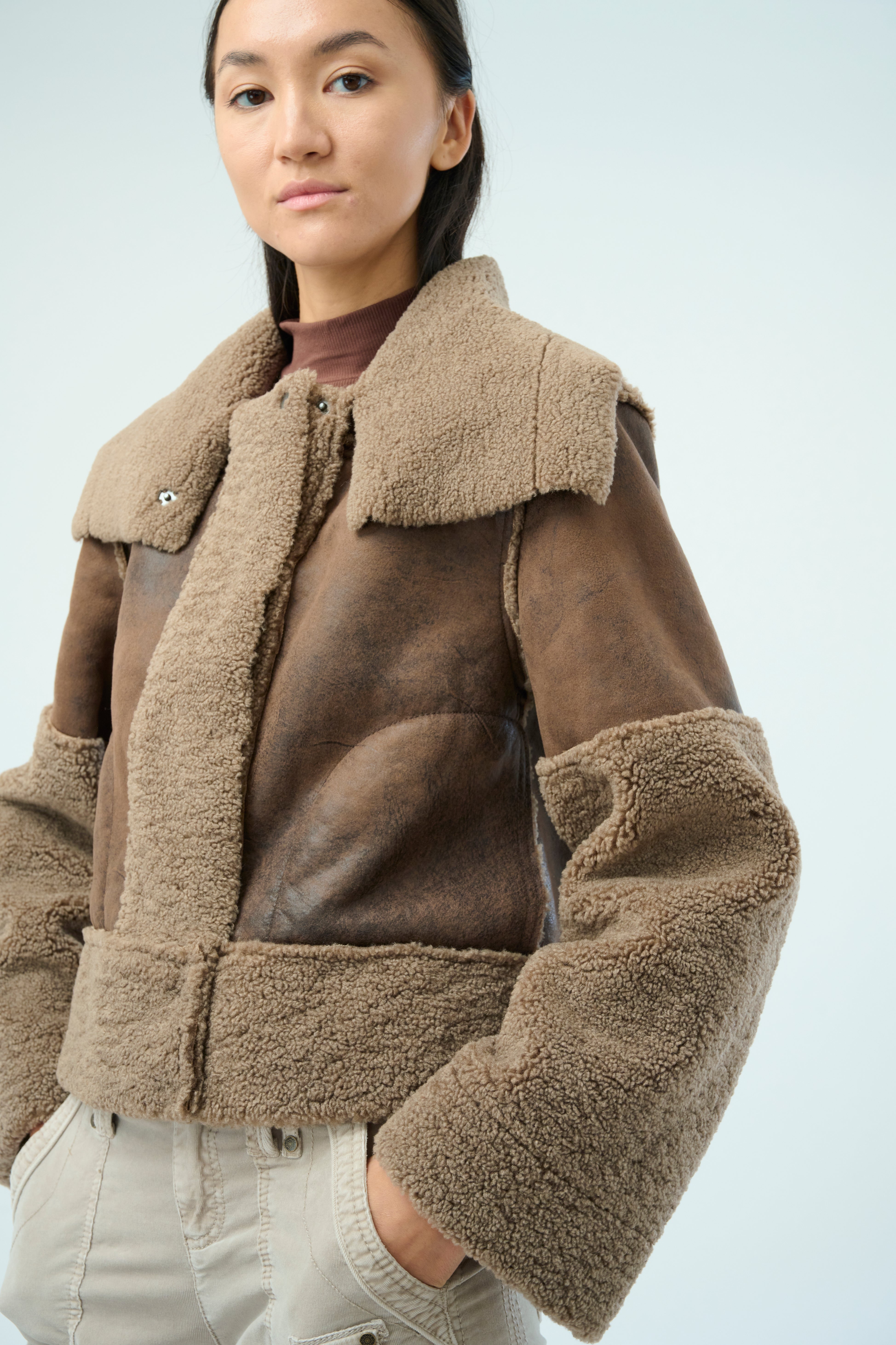 Front view of a tall female model with long black hair confidently posing wearing our hazel colored Trisha Bonded Distressed Suede Sherpa Jacket from Marrakech Clothing.