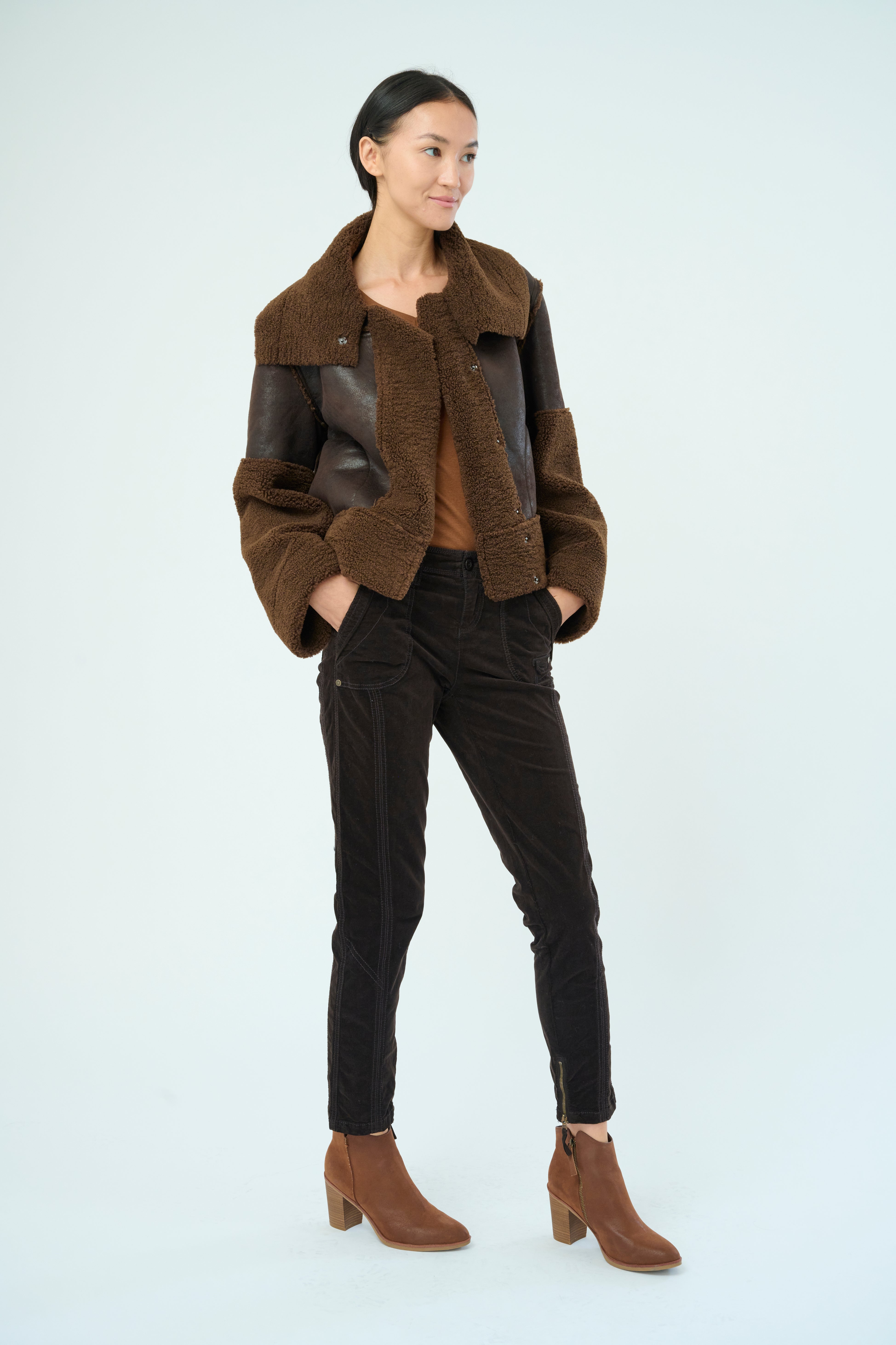 Front view of a tall female model with long black hair confidently posing wearing our dark chocolate colored Trisha Bonded Distressed Suede Sherpa Jacket from Marrakech Clothing.