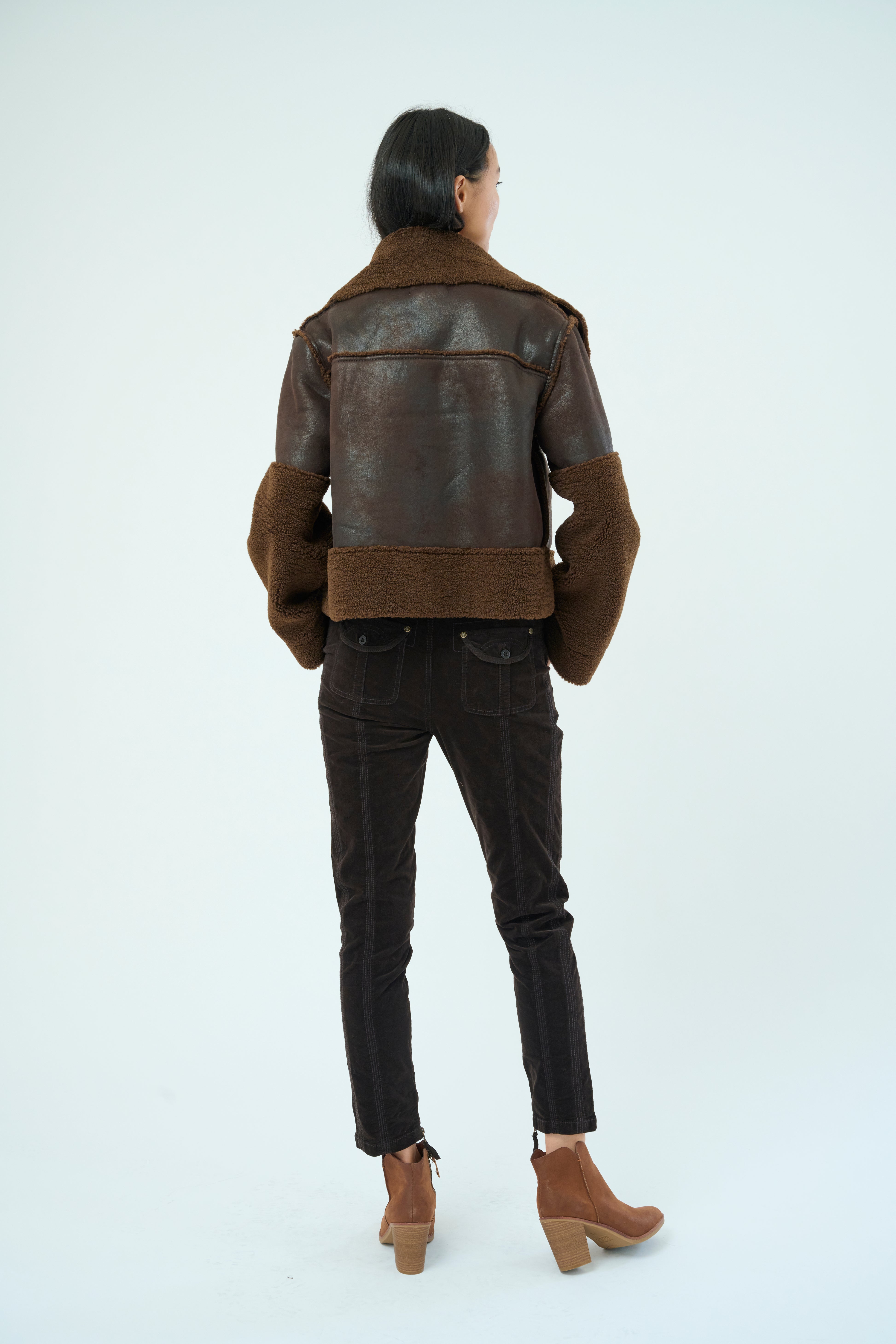 Back view of a tall female model with long black hair confidently posing wearing our dark chocolate colored Trisha Bonded Distressed Suede Sherpa Jacket from Marrakech Clothing.